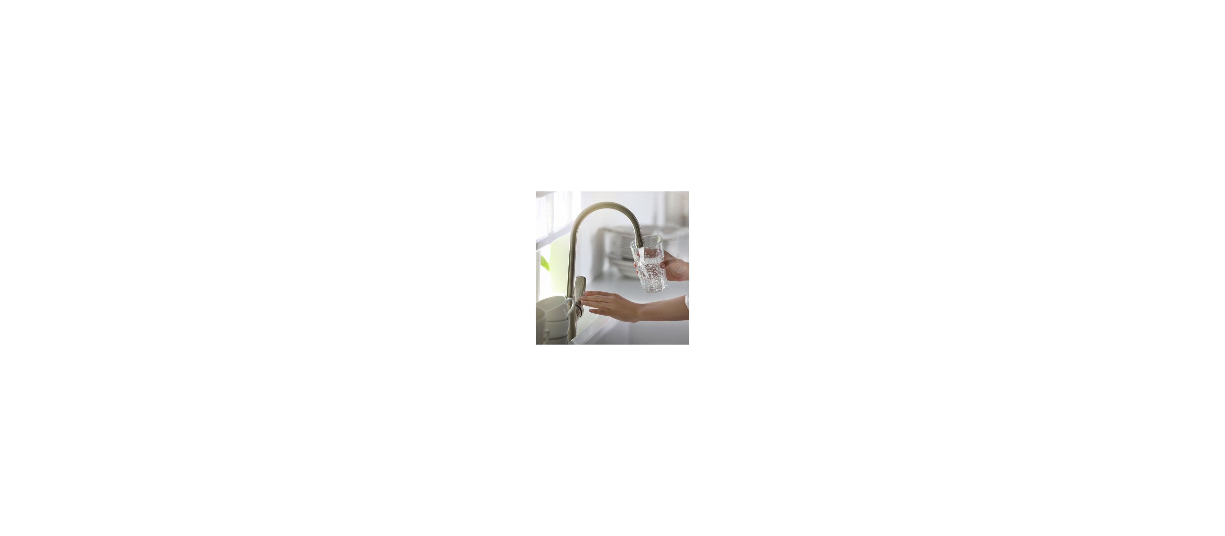 A glass of water is filled with tap water in a bright kitchen environment