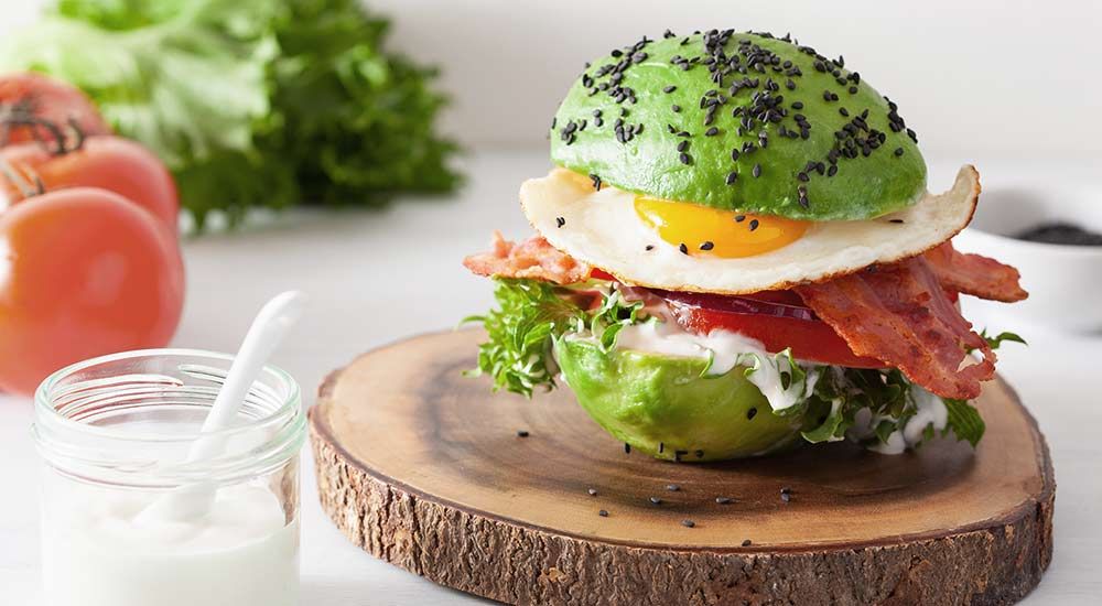 Avocado served as a sandwich, cut in the middle with egg, bacon and lettuce between the avocado halves