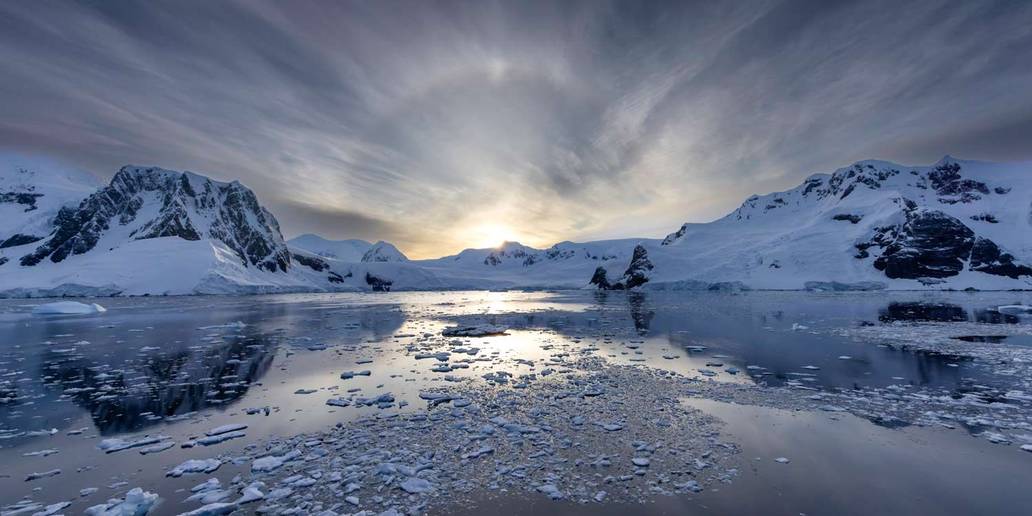 Sunset over icy Antarctic waters with snow-covered mountains in the background