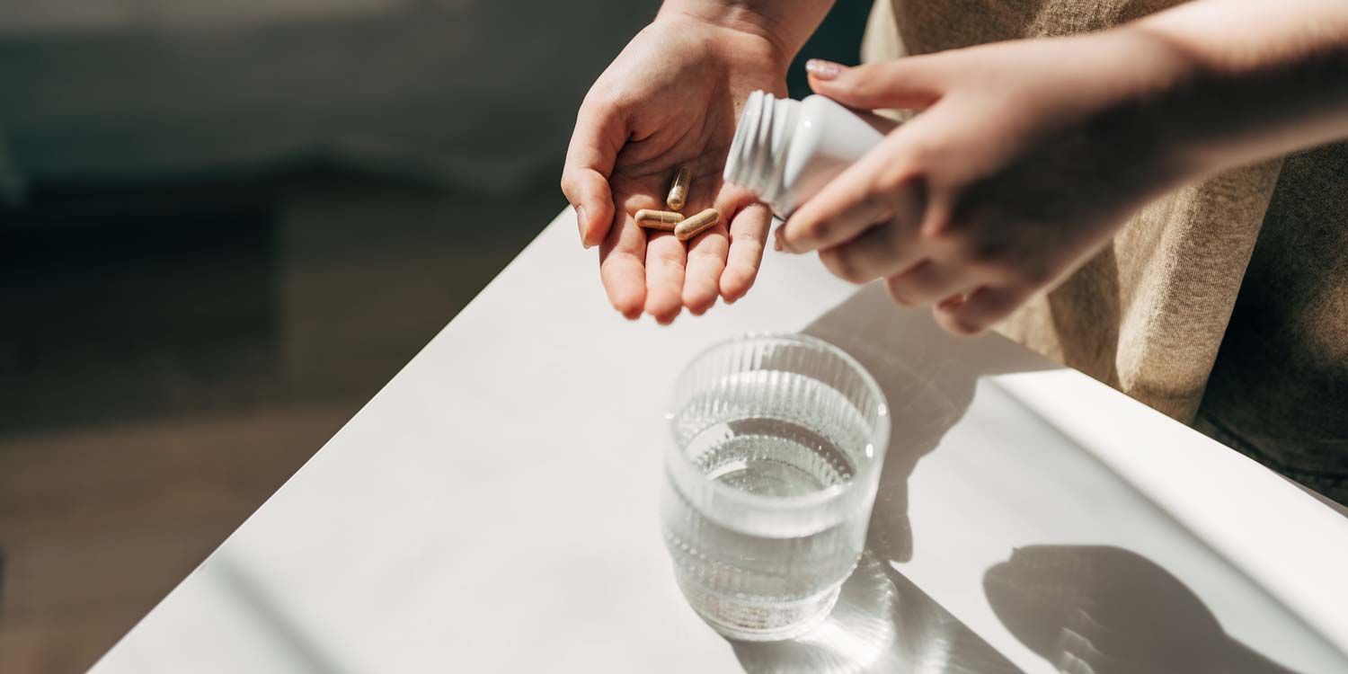 Capsules poured into a hand, with a glass of water next to it.