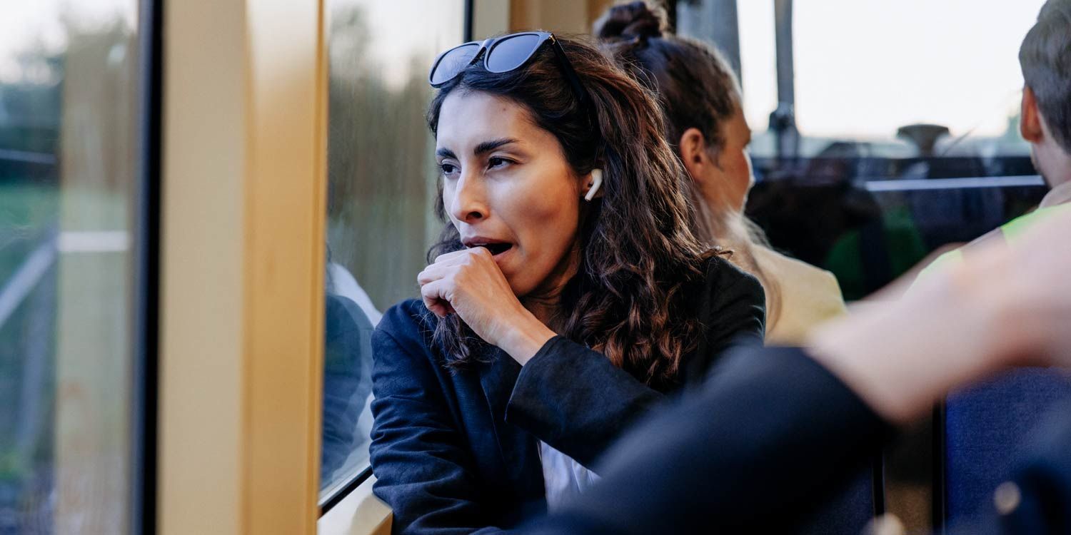 Kvinna sitter i kollektivtrafik, tittar ut genom fönstret och gäspar
