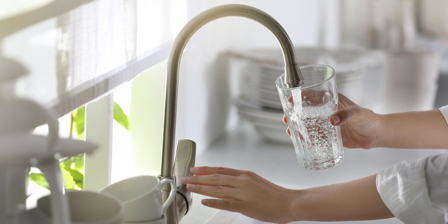 Ett glas vatten fylls med kranvatten i en ljus köksmiljö