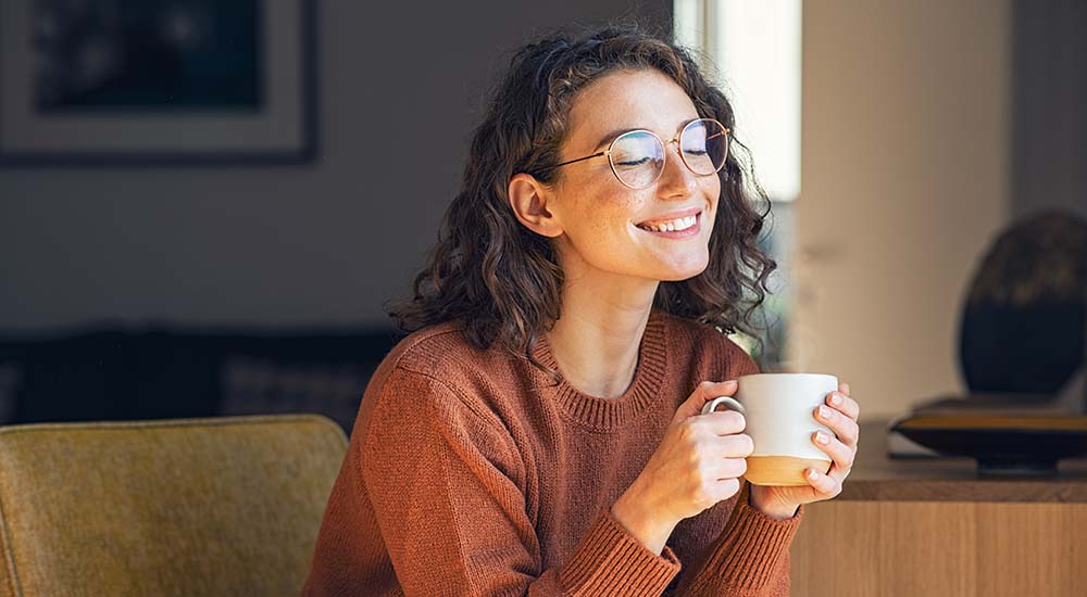 Happy woman enjoying a hot cup of tea in her home