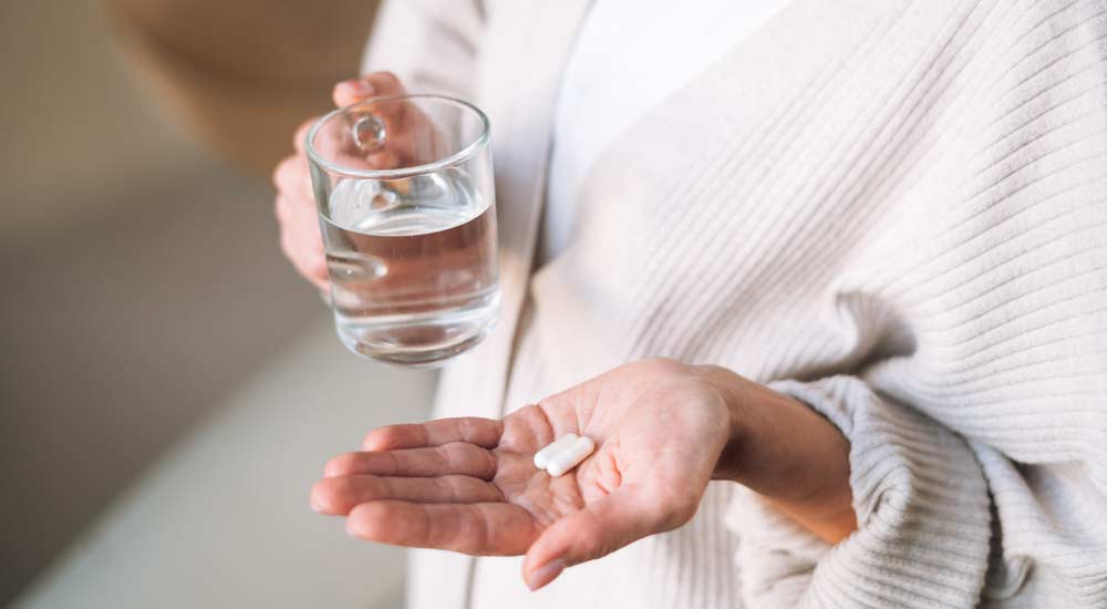 Woman with two capsules in one hand and a glass of water in the other