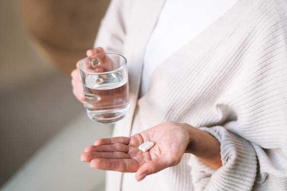 Woman with two capsules in one hand and a glass of water in the other
