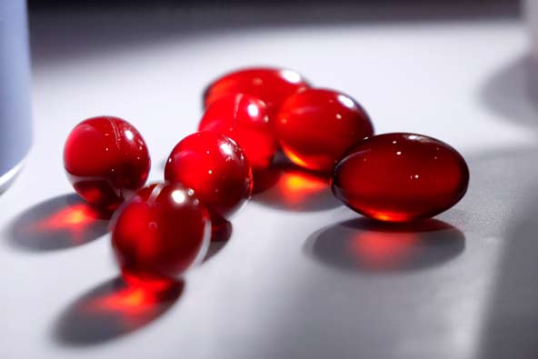 Close-up of red krill oil capsules on a white surface, lit warmly by sunlight shining through the capsules.