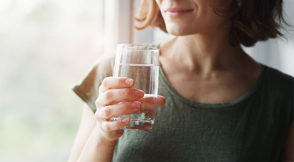 Kvinna håller ett glas klart vatten vid ett fönster i mjukt dagsljus