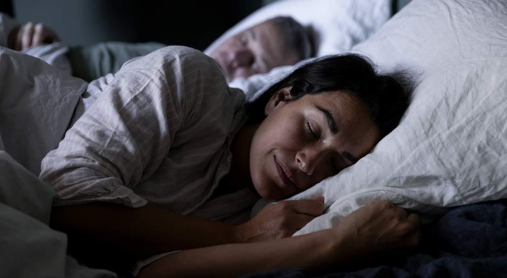 Kvinna sover gott i sängen bredvid sin man
