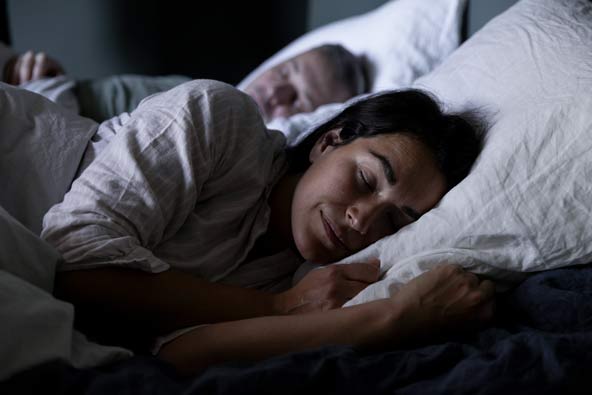 Kvinna sover gott i sängen bredvid sin man