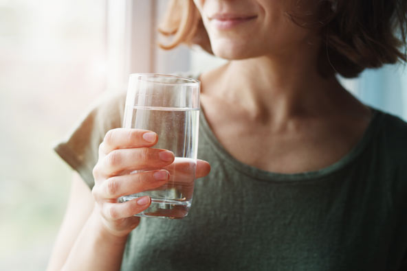Kvinna håller ett glas klart vatten vid ett fönster i mjukt dagsljus