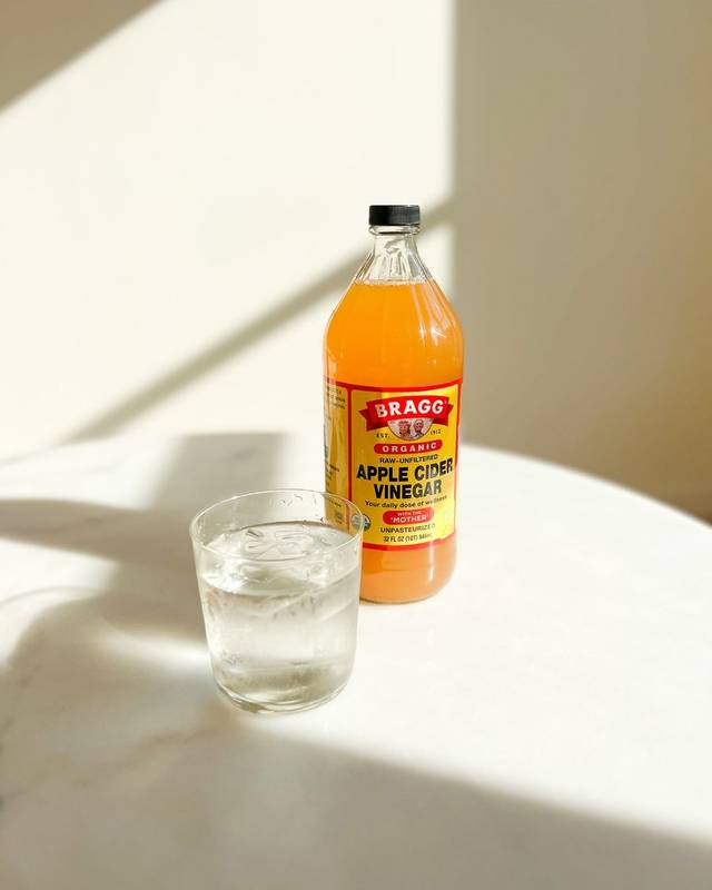 Bragg äppelcidervinäger bredvid ett glas vatten