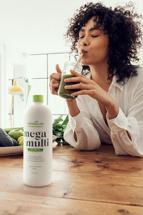 Kvinna dricker smoothie med en flaska N&auml;rok&auml;llan Mega Multi framf&ouml;r sig