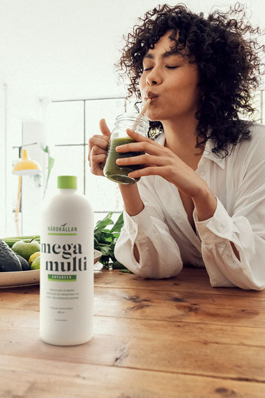 Kvinna dricker smoothie med en flaska N&auml;rok&auml;llan Mega Multi framf&ouml;r sig