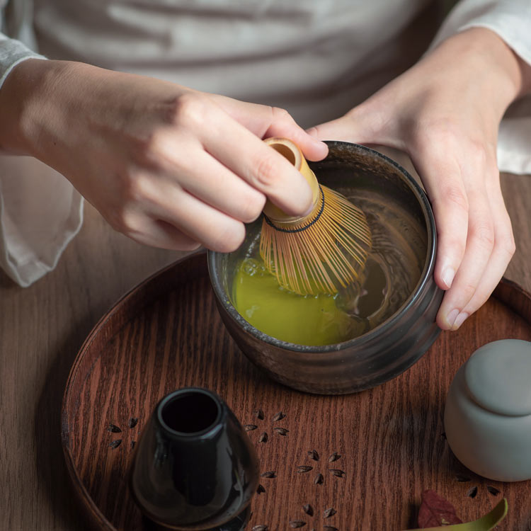 Hands whisking organic ceremonial matcha with a bamboo whisk.