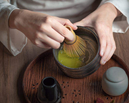 Hands whisking organic ceremonial matcha with a bamboo whisk.