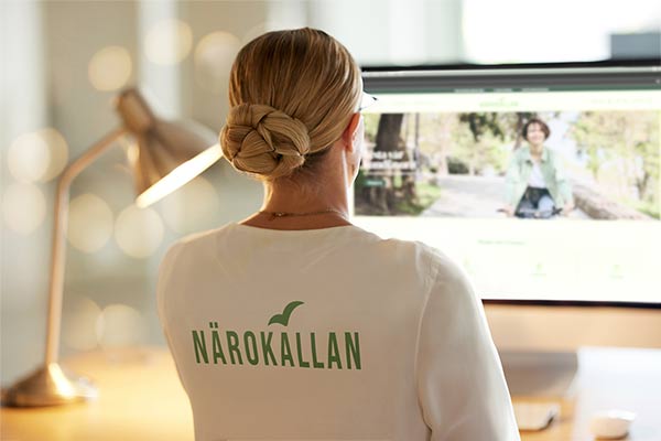 Woman in N&auml;rok&auml;llan shirt working at computer with website open.