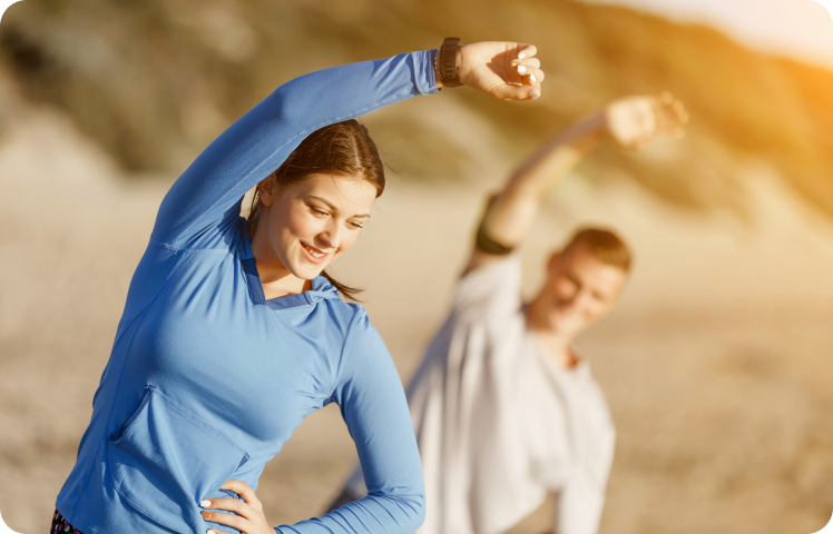 Woman stretching in the sun on the beach, man in background.